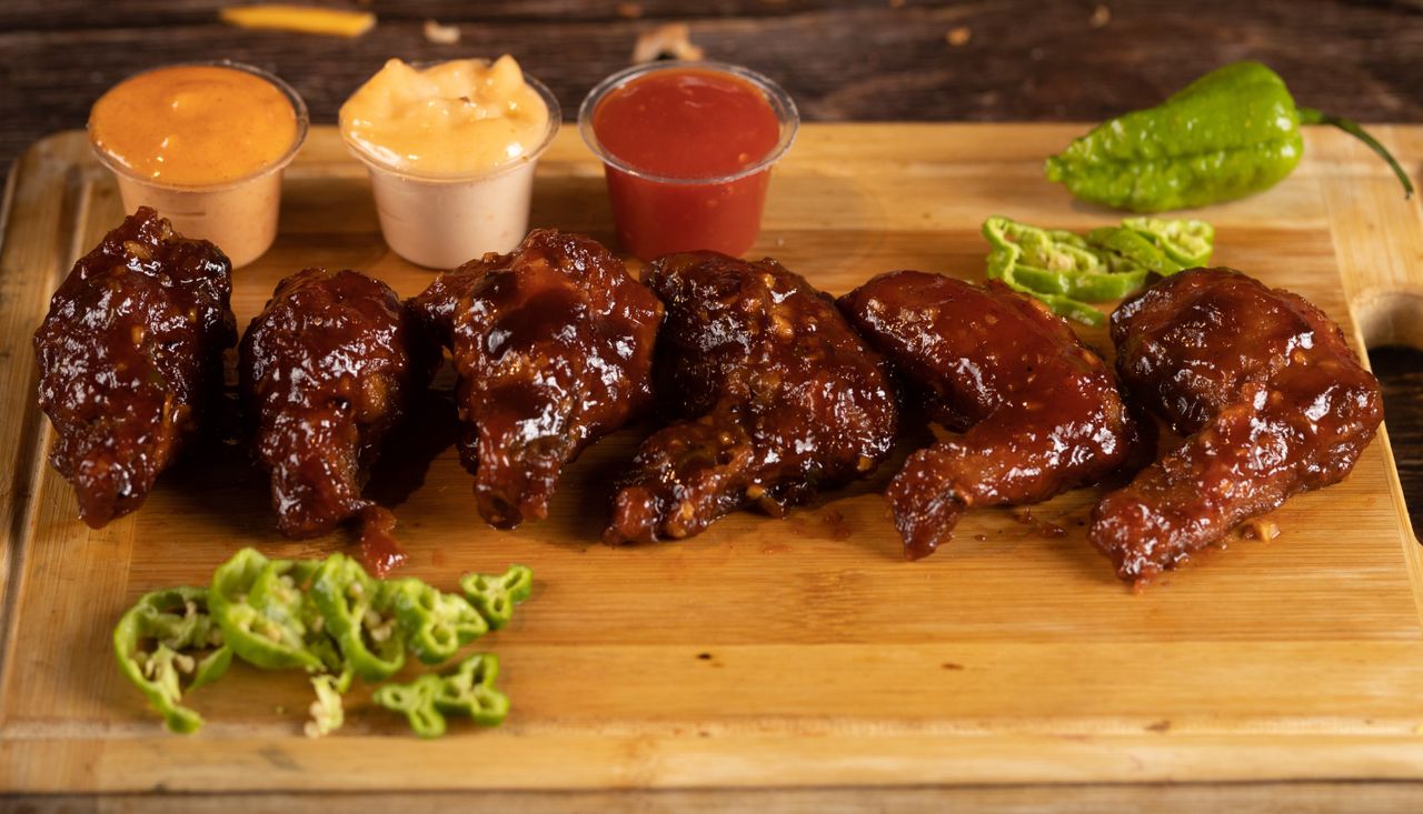 Mouthwatering barbecue chicken wings with dipping sauces on a wooden board.